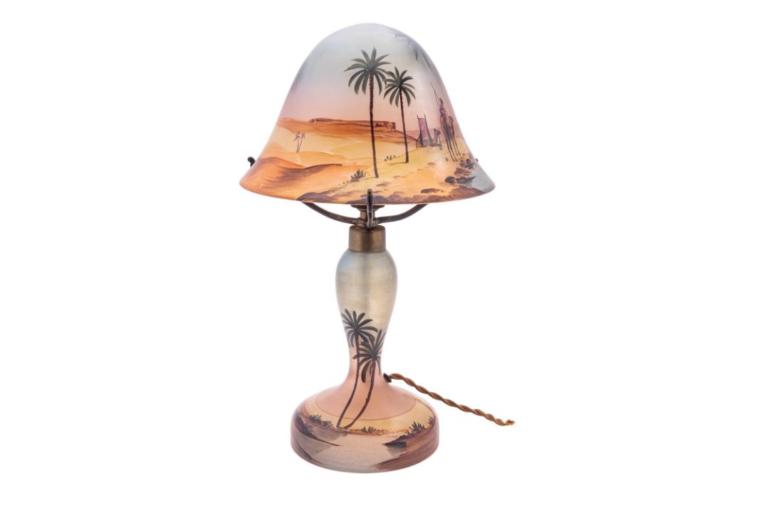 A painted glass table lamp and domed shade painted with a figure and camels at a desert oasis,