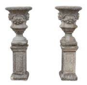 A pair of stone composition garden urns on plinths,
