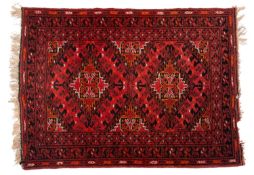 An Afghan Turkoman rug, the tomato red field with twin lozenge hooked medallions,