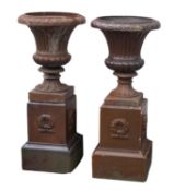 A pair of glazed stoneware garden urns on plinths,