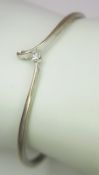 An 18K White Gold and Diamond Crossover Bangle with Solitary Diamond. Round brilliant cut