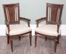 Pair of ornately carved wooden open armchairs, possibly Syrian in origin, with stuffed upholstered
