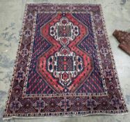 Eastern red ground rug with two central geometric hooked medallions, geometric spandrels and