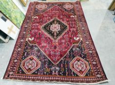 Large Eastern red ground rug with central lozenge on floral field, floral spandrels with geometric