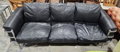 In the manner of Le Corbusier a three-seater sofa with black leather-effect upholstery, on a tubular
