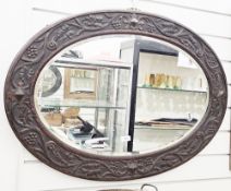Early 20th century oval bevelled edge wall mirror, the dark oak frame carved with foliate scrolls