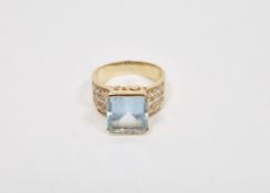Gold ring set with central emerald cut blue stone (possibly aquamarine) with diamond set