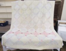 A patchwork quilt, mainly cream with touches of pink, pale blue, mauve etc., the whole is a bit