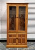 Ercol golden oak display cabinet, the upper section with two bevel glazed doors opening to three