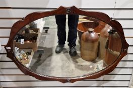 Early 20th century wall mirror of oval form, the walnut frame with wavy edge and applied flower