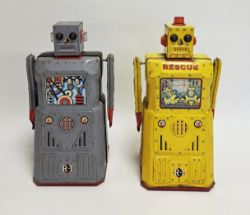 Two Rocket USA R-1 tinplate battery-powered robots, one in yellow rescue and the other with a