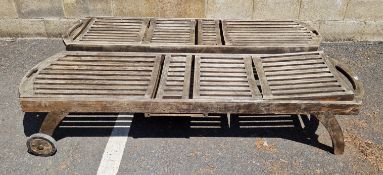 A pair of weathered two-wheeled teak slatted garden loungers, 203cm L x 63cm wide, excl. wheels
