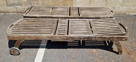 A pair of weathered two-wheeled teak slatted garden loungers, 203cm L x 63cm wide, excl. wheels