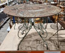 A scrolled wrought iron garden table with circular pierced top, painted pale green, 97cm dia x