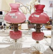 Pair of early 20th century cranberry glass and brass oil lamps with cranberry wells and shades