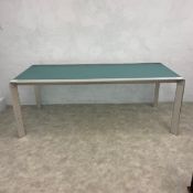 A vintage dining table with bent frosted plate glass top raised on canted brushed-metal supports.