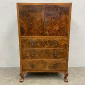A mid century Art Deco style burr walnut tallboy with figured cupboard doors enclosing two shelves