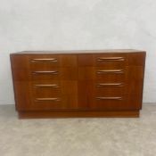 A mid-century teak sideboard or chest of eight drawers with scrolled handles raised on a square