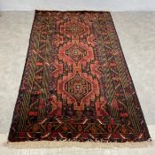 An Afghan Baluch carpet with stepped pole medallion and iron red flowerhead field over a charcoal