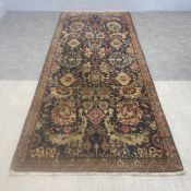 A Persian Kerman carpet runner with allover polychrome foliate field over a midnight ground within a