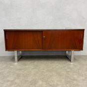 A mid-century teak sideboard with two slide doors enclosing shelves raised on bent chrome trestle