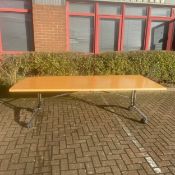 A vintage boardroom table with folding beech top raised on chrome trestle supports on castors by