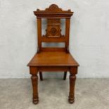 A late 19th century walnut hall chair with shaped and carved back-rail above panel seat raised on
