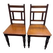 A pair of C.1900 walnut hall chairs with square openwork backs over the canted plank seats raised on