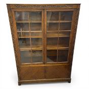 An early 20th century oak bookcase with carved frieze over the pair of astragal glazed cabinet doors