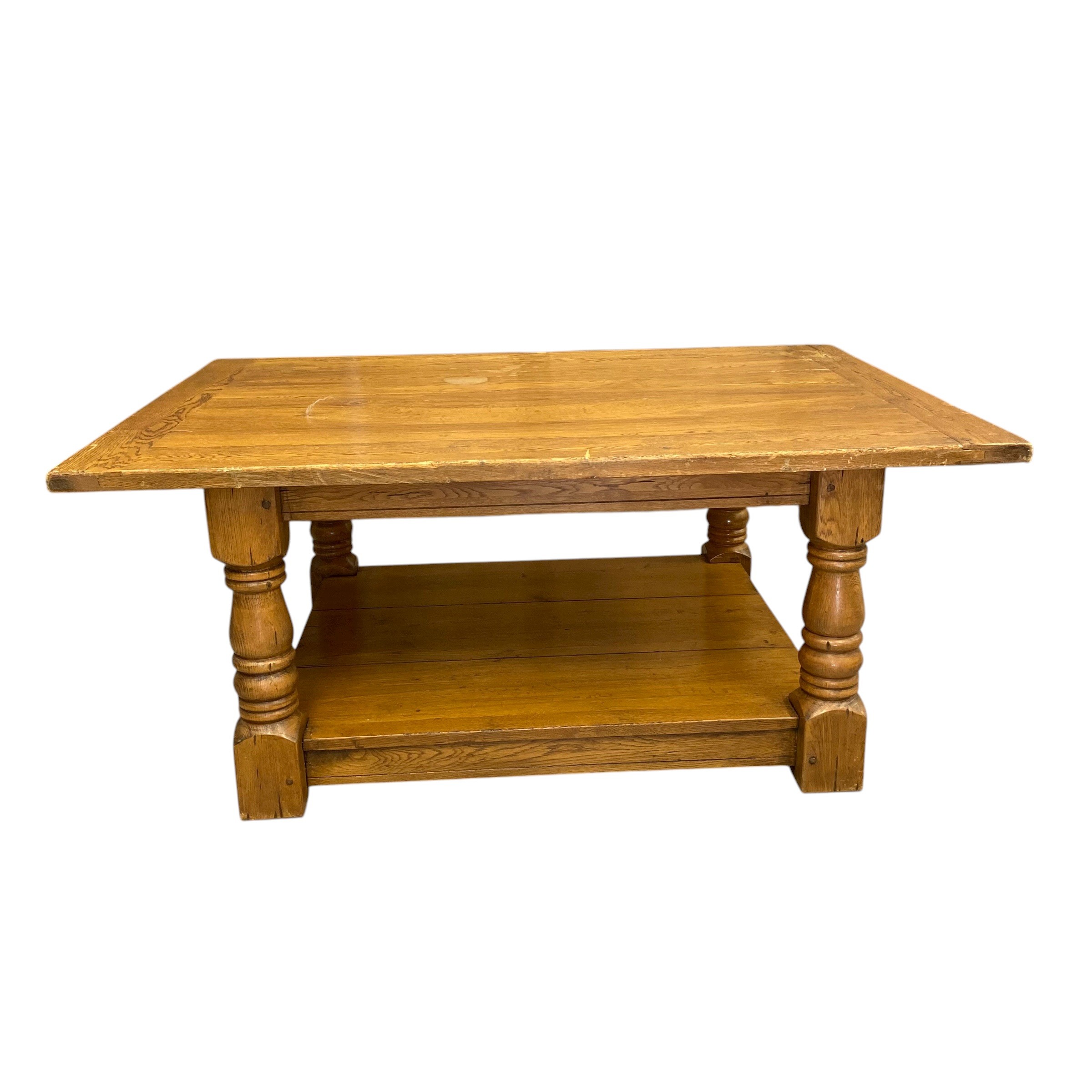 A vintage farmhouse style oak coffee table with plank top raised on heavy turned supports united