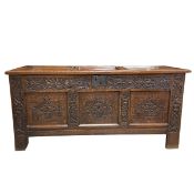An 18th century oak coffer with panel top enclosing a candle box over the carved frieze raised on