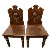 A pair of mid 19th century walnut hall chairs with broken pediment and carved back over the plank