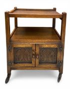 A mid 20th century two-tier oak serving trolley with galleried top over carved panel cabinet doors