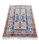A contemporary Kazak style rug with three geometric diamond lozenge medallions over a peach ground