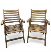 A pair of vintage campaign style folding teak garden armchairs with slatted backs and scrolled