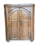 A 19th century oak corner hanging wall cabinet with a dentil moulded cornice over arched panel doors