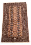 A Persian Bokhara rug with two rows of fourteen guls over a pale red abrash ground within multiple
