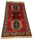 A Caucasian Kazak style carpet with three polychrome medallions over a box red ground within