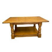 A vintage farmhouse style oak coffee table with plank top raised on heavy turned supports united