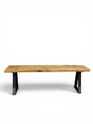 A contemporary Brutalist style bench with raw distressed oak seat raised on industrial steel trestle