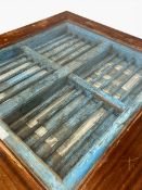 A teak dining table with inset distressed painted window grille under a plate glass top. H.76 x W.