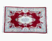 A Chinese Aubusson style woollen carpet with central foliate medallion on a deep burgundy ground and