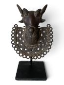 A 19th century Benin bronze hip mask in the form of a stylised ram's head. H.19cm on stand.