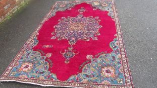 A large Oriental style woollen rug in red, green and blue colourway, with fringe