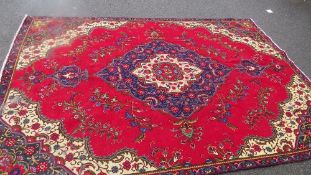 A large Oriental style woollen rug in red, green and blue colourway, with fringe