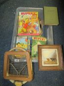 A tray of sundries to include a framed Crown Devon Highland cow tile, Rupert annuals etc