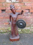 A CARVED BURMESE HARDWOOD STATUE OF A FIGURE IN TRADITIONAL DRESS, holding a gong in one hand and