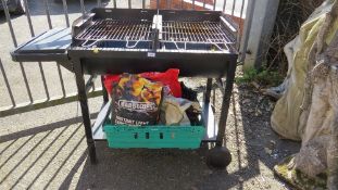A large dual burner charcoal barbeque with wheels and bags of charcoal