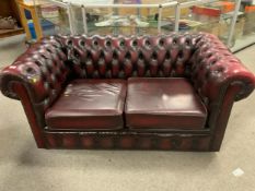 An oxblood red leather two seater Chesterfield settee