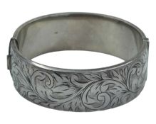 A heavy silver hinged bangle with foliate scroll engraved decoration.
